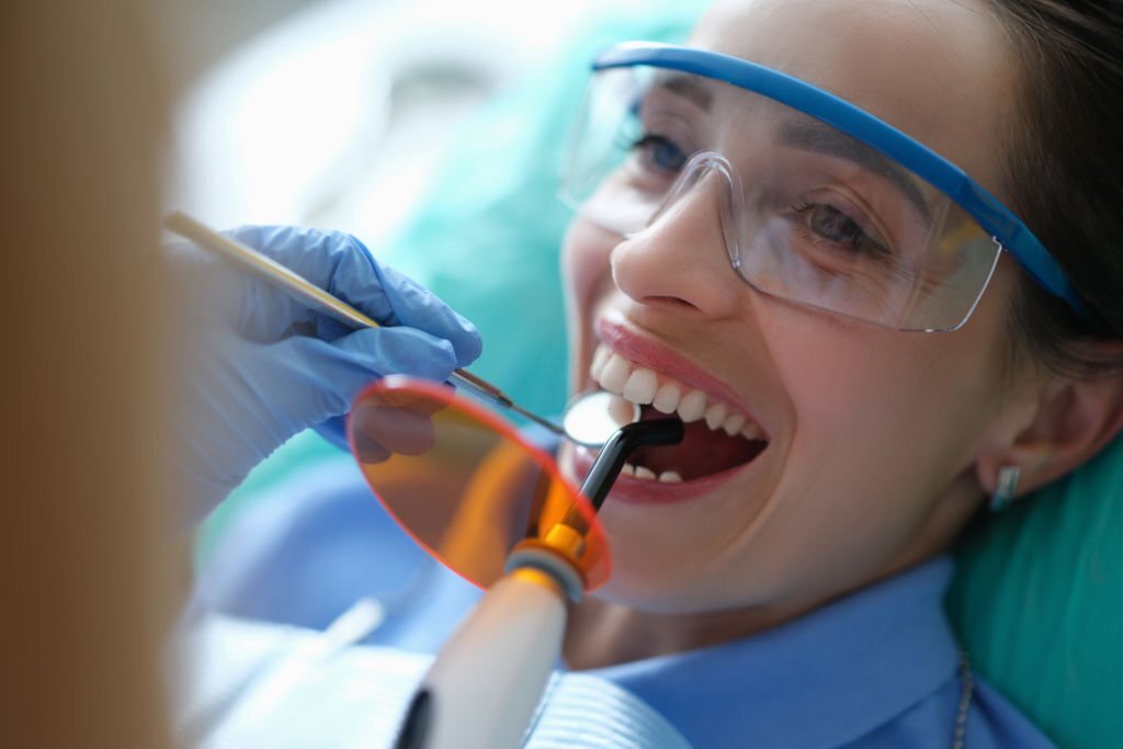 Doctor dentist treating teeth using LED curing light machine in clinic closeup. Modern technologies in dentistry concept